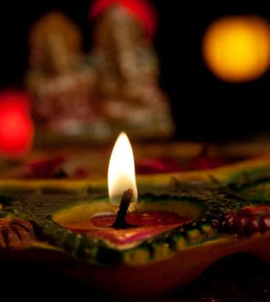 blurred Ganesha Idol behind burning diya